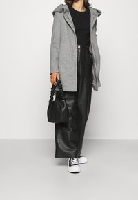 Grå ullkappa med huva, ihop med en svart stickad topp, svarta konstläderbyxor och en liten svart väska. Vita sneakers fulländar outfiten.