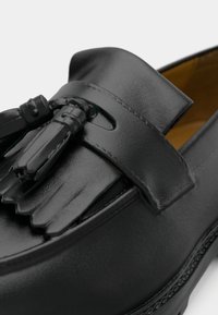 Zwarte leren loafers met een gladde afwerking, kwastje detail en een ronde neus. Klassiek ontwerp met minimale stiksels.