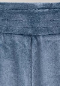 Gros plan d'un tissu polaire doux bleu montrant une ceinture cousue et une couture verticale en dessous.