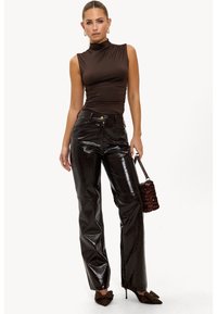 Femme portant un col roulé sans manches marron, un pantalon taille haute noir brillant, des talons aiguilles marron avec des nœuds, et tenant un sac à main en sequins marron.