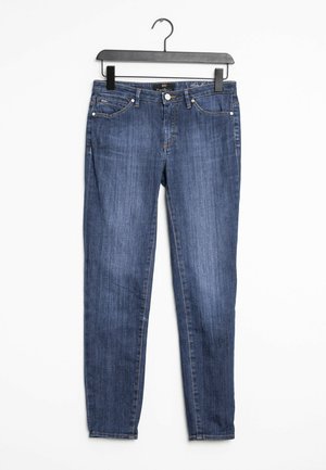 Jean slim bleu suspendu sur un cintre noir contre un fond blanc, avec des détails de boutons et poches à l'avant.