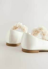 Ballerines en satin blanc avec un bout rond, ornées d'une sangle décorée de fleurs en tissu beige clair et d'une semelle douce.
