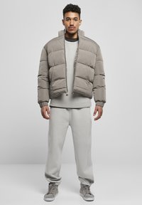 Lys grå pufferjakke med en cropped design, lynlåslukning foran og to forlommer. Båret over en struktureret lys grå sweater og matchende svedbukser.