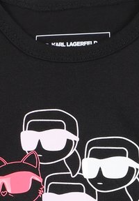 T-shirt nera in cotone con figure di cartone stilizzate bianche e rosa che indossano occhiali da sole, tra cui un gatto con accenti rosa.