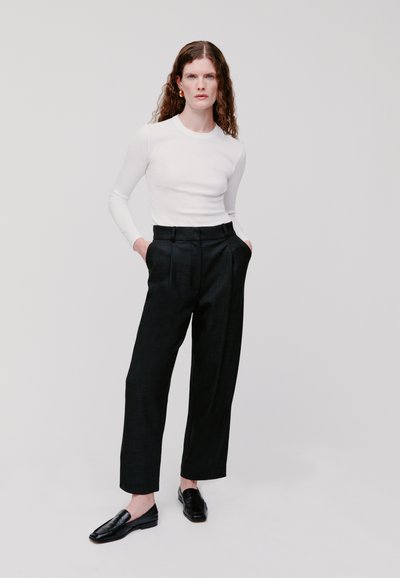 Top attillato bianco a maniche lunghe abbinato a pantaloni neri a vita alta. Muffole nere completano l'outfit, creando un look elegante e minimalista.