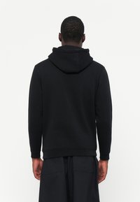 Zwarte hoodie met een gladde textuur, ribgebreide boorden en een kangoeroezak, gecombineerd met donker losse shorts.