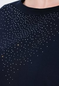 T-shirt blu navy con un motivo disperso di piccoli strass argentati, che creano una texture sottile e un dettaglio luccicante.