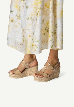 Sandales plateforme beiges avec découpes circulaires et bride à la cheville. Semelle compensée texturée avec motif ondulé. Design à bout ouvert.