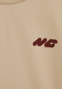 Tissu beige avec les lettres stylisées "NG" en rouge foncé imprimées en bas à droite.