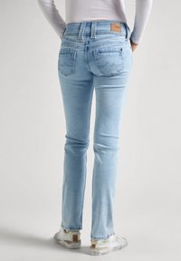 Ljust blå denimjeans med slim fit, två bakfickor och en läderlapp vid midjan. Bärs med vita sneakers.