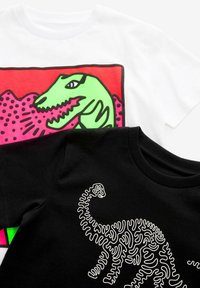 Divas T-krekli: viens balts ar spilgti zaļu dinozaura grafiku uz sarkana fona, un otrs melns ar baltu dinozauru dizainu, kas atgādina puzli.