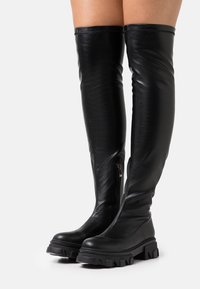 Black leather over-the-knee boots with a smooth texture, rounded toe, chunky treaded sole, and side zipper detail.
