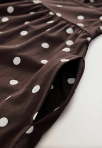 Rochie din țesătură maro, cu buline mari albe, având talie strânsă și mâneci scurte, care evidențiază o textură netedă și un design casual.