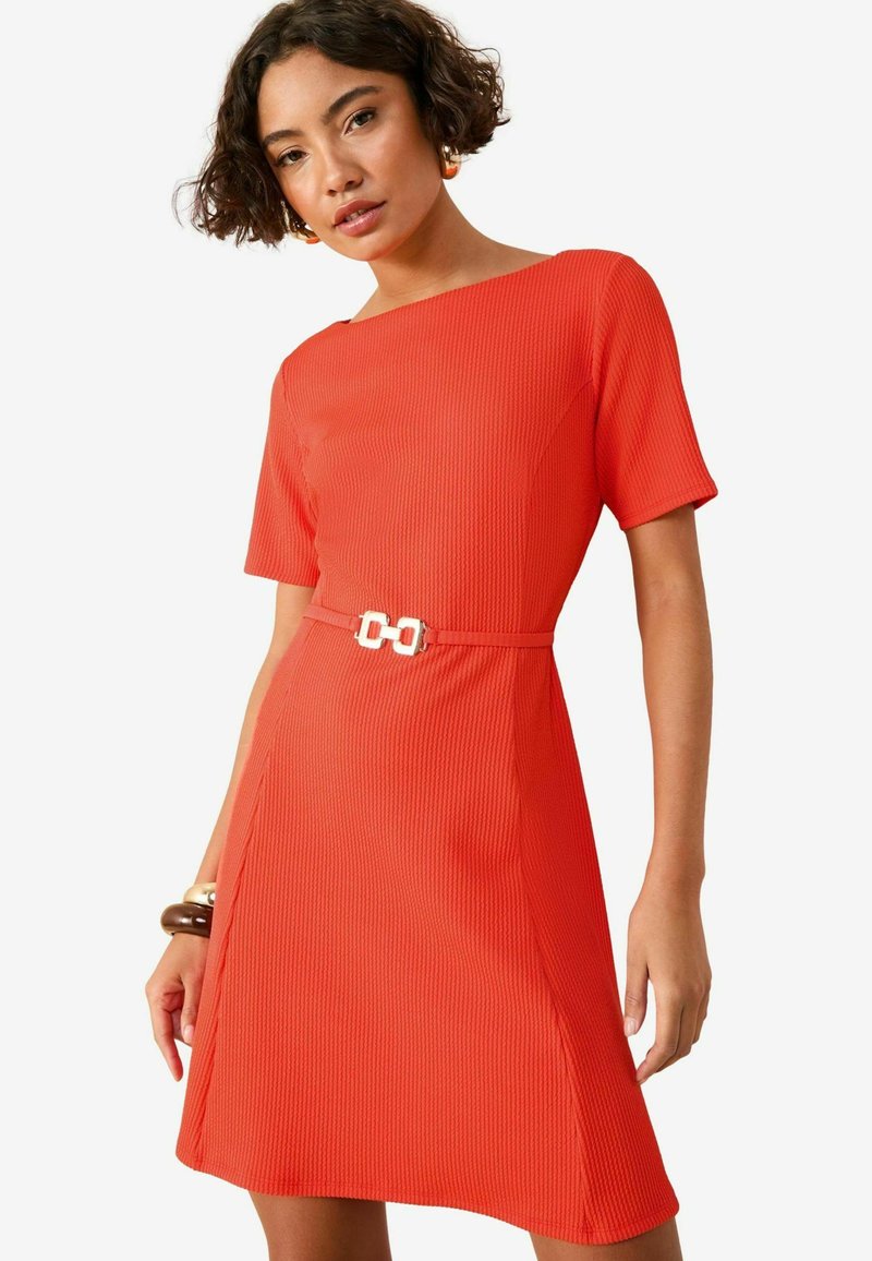 Vestido rojo con manga corta, escote redondo y un cinturón blanco con hebilla decorativa. De longitud media y silueta en A.