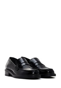 Mocasines de cuero negro con un acabado suave, punta redondeada y una tira decorativa en la parte superior. Tacón bajo y grueso. Diseño simple y clásico.