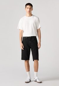 Črne denim kratke hlače z ravnim krojem, kombinirane z ohlapno belo bombažno majico. Dodatki vključujejo bele nogavice in superge.