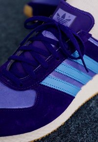 Violet sportinė avalynė su mėlynomis juostelėmis, pagaminta iš veliūro ir tekstilės medžiagų, tekstūruotas paviršius ir balta guma, su tekstūruotu padu.