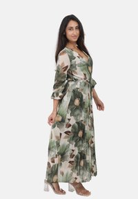 Robe maxi en tissu léger et fluide avec un motif de feuilles vertes et de fleurs. Présente un design enroulé et une taille ceinturée, complétée par des manches 3/4.