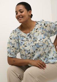 Blusa floreale multicolore con motivi blu, neri e gialli, maniche corte a palloncino e una morbida texture plissettata.