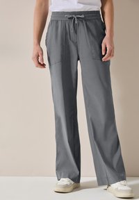 Grijze wijde broek met een verstelbare tailleband, voorzien van twee voorzakken, gemaakt van een lichtgewicht stof. Gekoppeld aan witte sneakers.