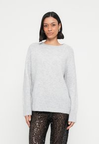 Hele hall, liiga suur kampsun pehmest kudumist, soonikkoes ääre ja laiade varrukatega, kombineeritud mustade litritega retuusidega.