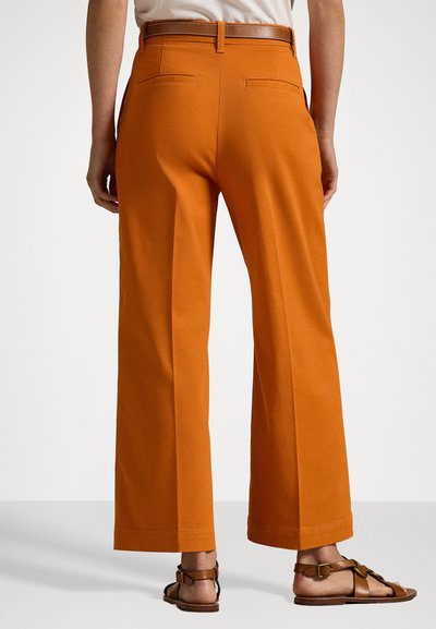 Wide-leg trousers in orange cotton with a high waist. Features back pockets and a smooth texture. Worn with brown sandals.