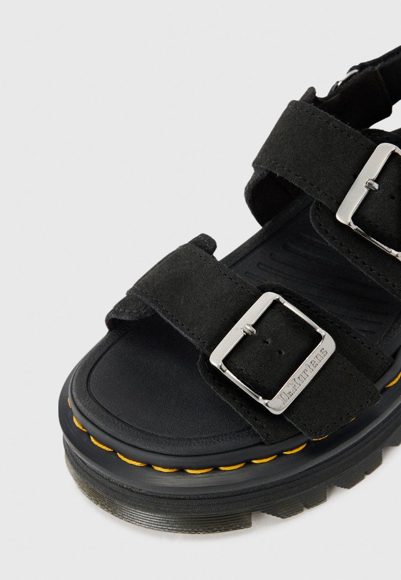 Sandalo in suede nero con cinturini regolabili, fibbie argentate e suola in gomma spessa con un'accenno giallo cucito. Soletta strutturata.
