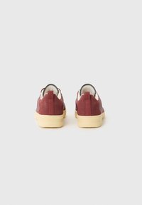 Maroon sneakers with a textured upper, featuring a cream collar and a beige rubber sole. Slip-on design with reinforced heel tabs.