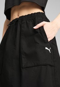 Svarta shorts av texturerad tyg med elastisk midja och en sidficka med en vit Puma-logga.