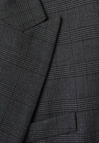 Tela a cuadros gris con un patrón clásico de espiga. La textura es tejida, con tonos de gris oscuros y claros en líneas entrelazadas.