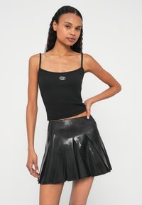 Juoda ribuota liemenė su plonais petnešėliais ir mažyčiu sidabriniu logotipu, derinama su blizgios medžiagos juodu raukšlėtu mini sijonu.