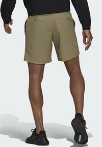 Khaki-short med elastisk midjeband, sidofickor och ett lätt, texturerat tyg, tillsammans med svarta träningsskor.