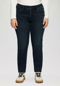 Ciemnoniebieskie jeansy o slim fit, pięć kieszeni i subtelne przeszycia. Połączone z kremowymi i brązowymi trampkami.