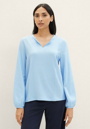 Blouse bleu clair avec des rayures verticales subtiles, manches longues et décolleté en V. Fabriquée en tissu doux avec une texture lisse.