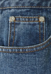 Tmavě modré džíny z denimu s malou přední kapsou se stříbrným knoflíkem a kontrastním oranžovým prošitím podél švů.