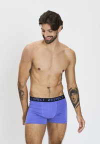 Boxer da uomo color viola con una fascia nera etichettata "RISPETTO". Il tessuto appare morbido e texture, aderendo comodamente attorno alla vita e cosce.