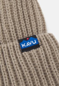 Beige kudumüts vertikaalse soonikuga, musta ja sinise KAVU logo plaastriga punaste aktsentidega. Pehme tekstuur, loodud sooja hoidmiseks.