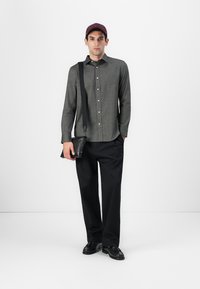 Grå skjorte med knapper, svarte bukser, svarte sko, rød caps, og en crossbody veske; har en subtil tekstur og en klassisk passform.