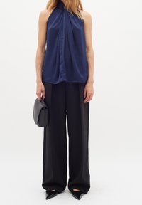 Marinblå halterneck-topp med draperad frontdetalj, i kombination med lösa svarta byxor och svarta klackskor med spetsig tå, kompletterat med en svart kuvertväska.