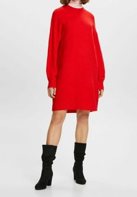 Czerwona dzianinowa sukienka swetrowa z długimi rękawami, okrągłym dekoltem i prążkowanymi mankietami. W połączeniu z czarnymi, luźnymi botkami na wysokim obcasie.