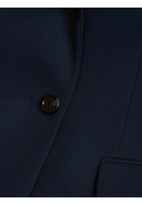 Mörkblå kavajtyg med en slät textur, som har en enkel svart knapp och en ficka med kant. Slimmad passform med rena linjer och sömmar.