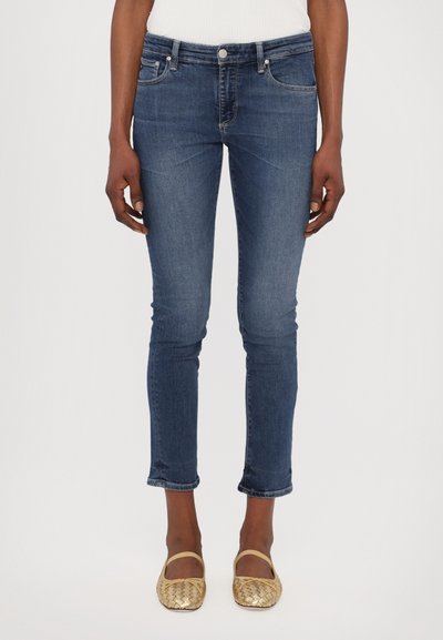 Chude jeans w ciemnoniebieskim dżinsie, z średnim stanem, pięcioma kieszeniami i lekkim przetarciem na hemie. W zestawie z plecionymi złotymi balerinkami.