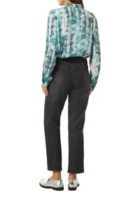 Langärmlige Bluse in Teal und Grau mit Muster, kombiniert mit hochtaillierten schwarzen Jeans und silbernen Slippers.