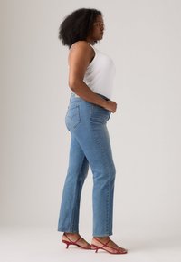 Lys blå denimjeans med rett benpassform, med et klassisk baklomme-design og en teksturert hvit tanktop. Røde stroppesandaler.