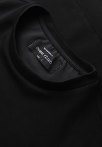 T-shirt noir à col rond avec une étiquette visible au niveau du col indiquant la marque Ombre Exmio et la taille large.