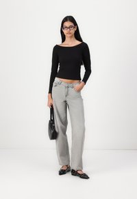 Black long-sleeve top, light gray wide-leg jeans with pockets, black flat shoes with cut-out details, and a small black handbag.