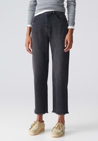 Jeans de mezclilla negra con un ajuste relajado, dobladillo deshilachado y cinco bolsillos. Combinados con zapatos de color beige claro.