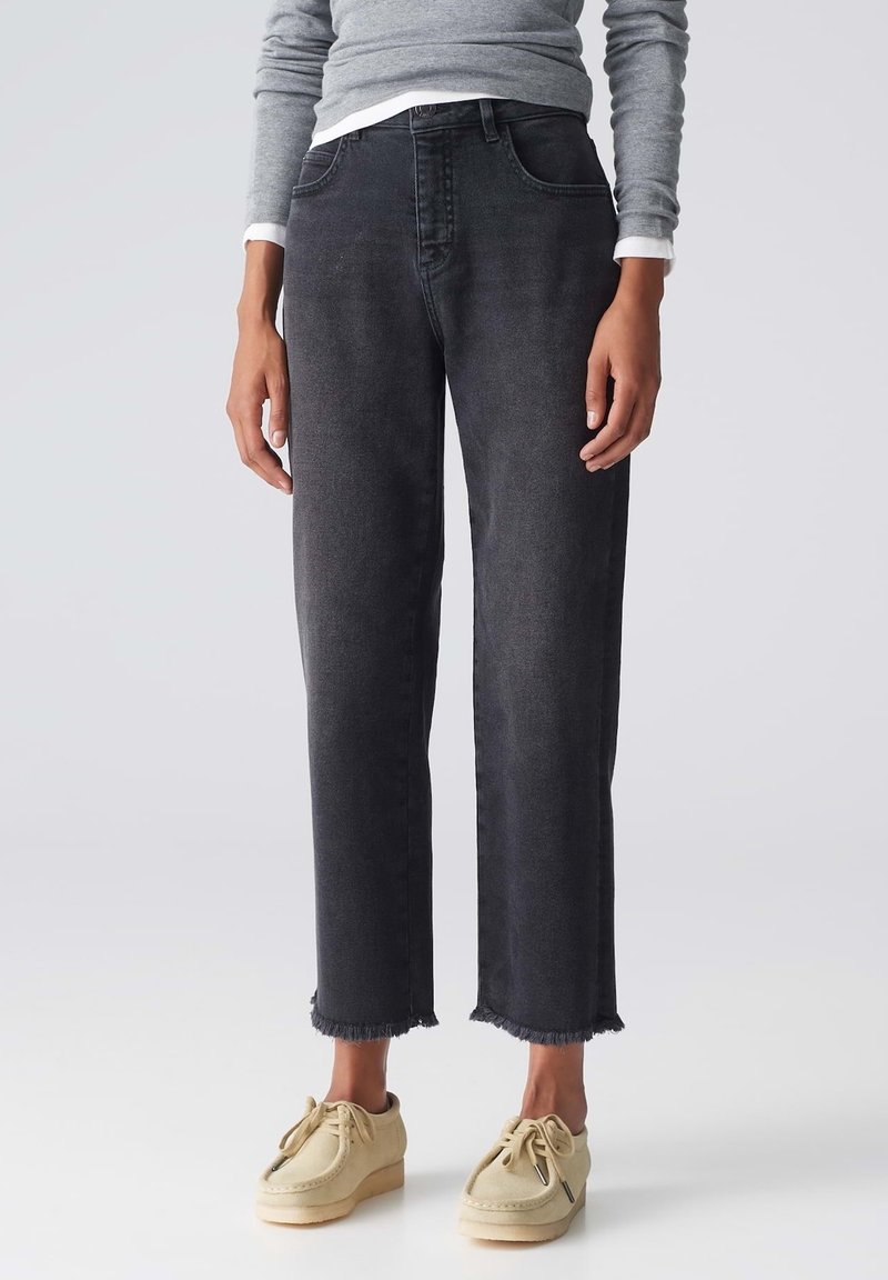 Jeans de mezclilla negra con un ajuste relajado, dobladillo deshilachado y cinco bolsillos. Combinados con zapatos de color beige claro.