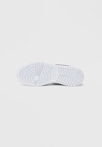 Czarny sneaker z białą gumową podeszwą, posiadający okrągłe i liniowe wzory bieżnika oraz logo. Gładka tekstura z opływowym designem.