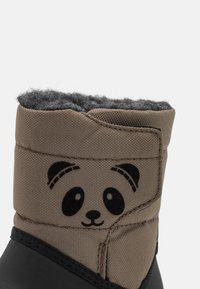 Hnědá textilní bota s černou gumovou podešví, která má šedou flísovou podšívku a design obličeje pandy na horní části.